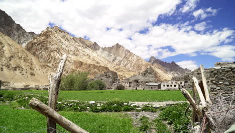 Pull-back-shot-between-a-fence-at-Hankar,-ghost-city-in-the-Himalayas-buildings-at-the-leg-of-mountains-on-a-bright-day