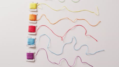 video of six bobbins of colourful embroidery threads unwound on white background