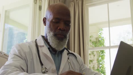 médico afroamericano de alto rango que usa una computadora portátil en casa