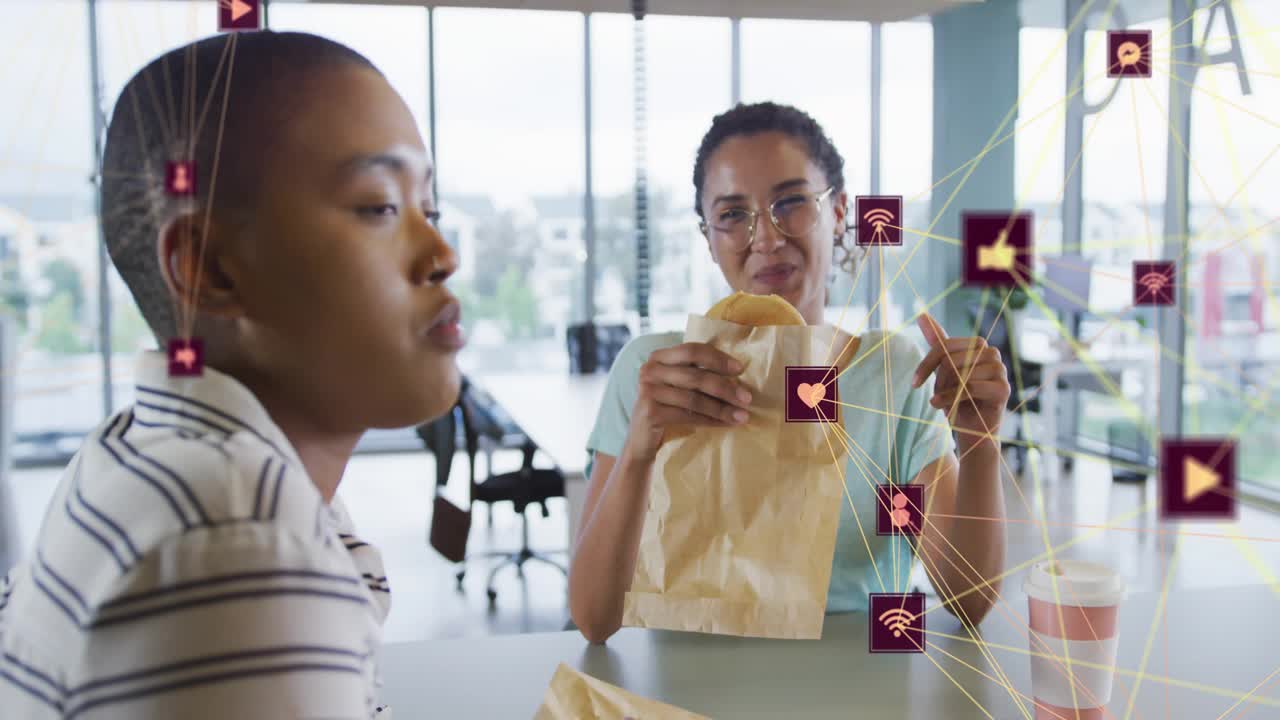 Teal-shirt woman taking bite and friend chatting with floating icons tracking social engagement