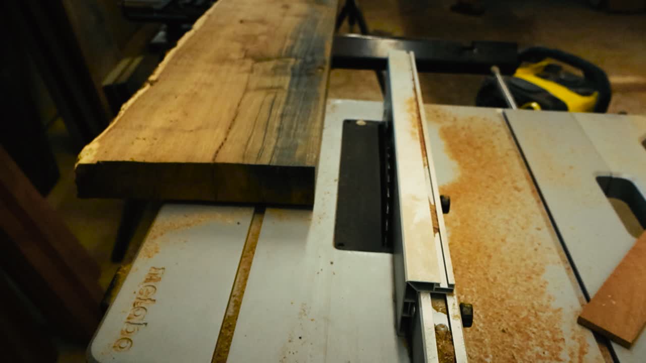 Top down view of a finely cut oak slab with deep colorful textures and details on a table saw where the blade is visible in the saw dust and woodchips. The dry plank or slab is ready to cut, workshop