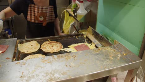 comida callejera taiwanesa frita en una parrilla de hierro plano por una mujer que contiene huevo, jamón, queso y tortitas de cebolla verde