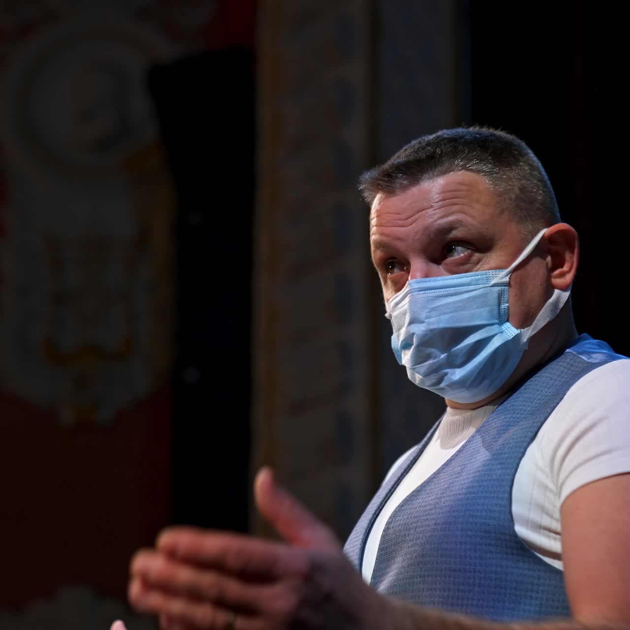 Man with medical mask in hands standing on stage and speaks seriously. Rehearsal during covid-19