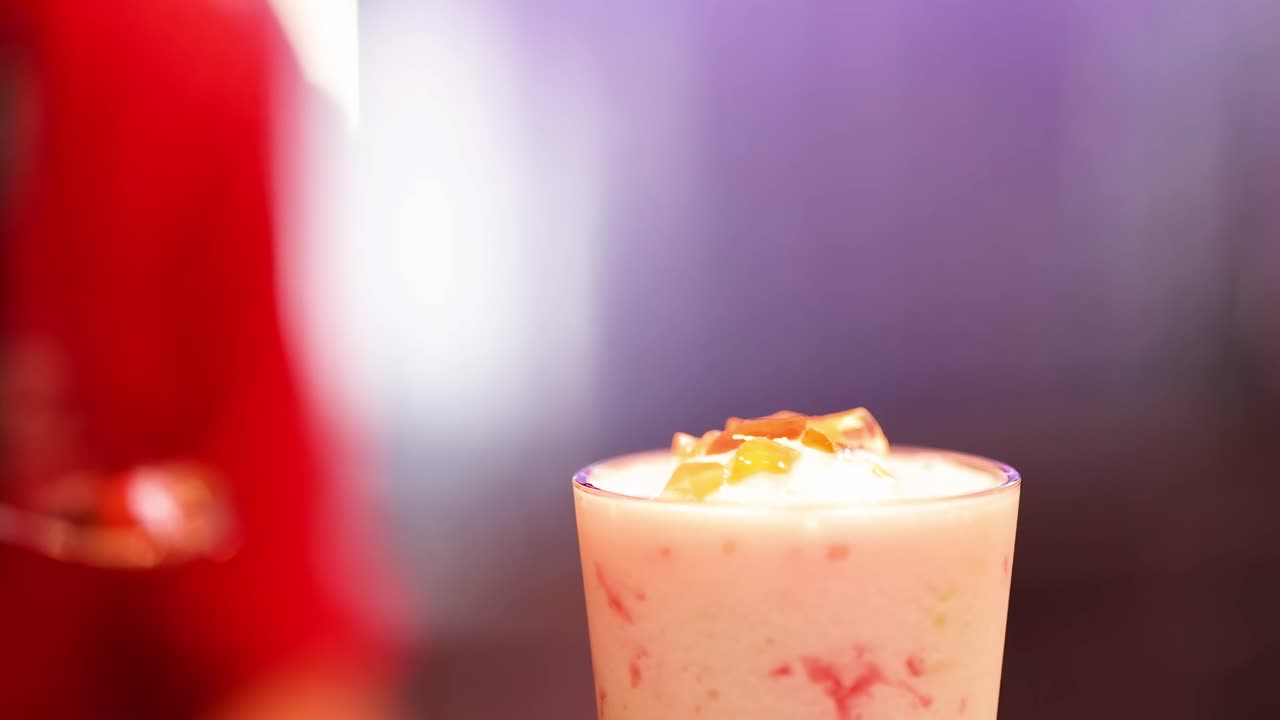 A close-up of a spoon adding toppings to a creamy drink in a red setting.