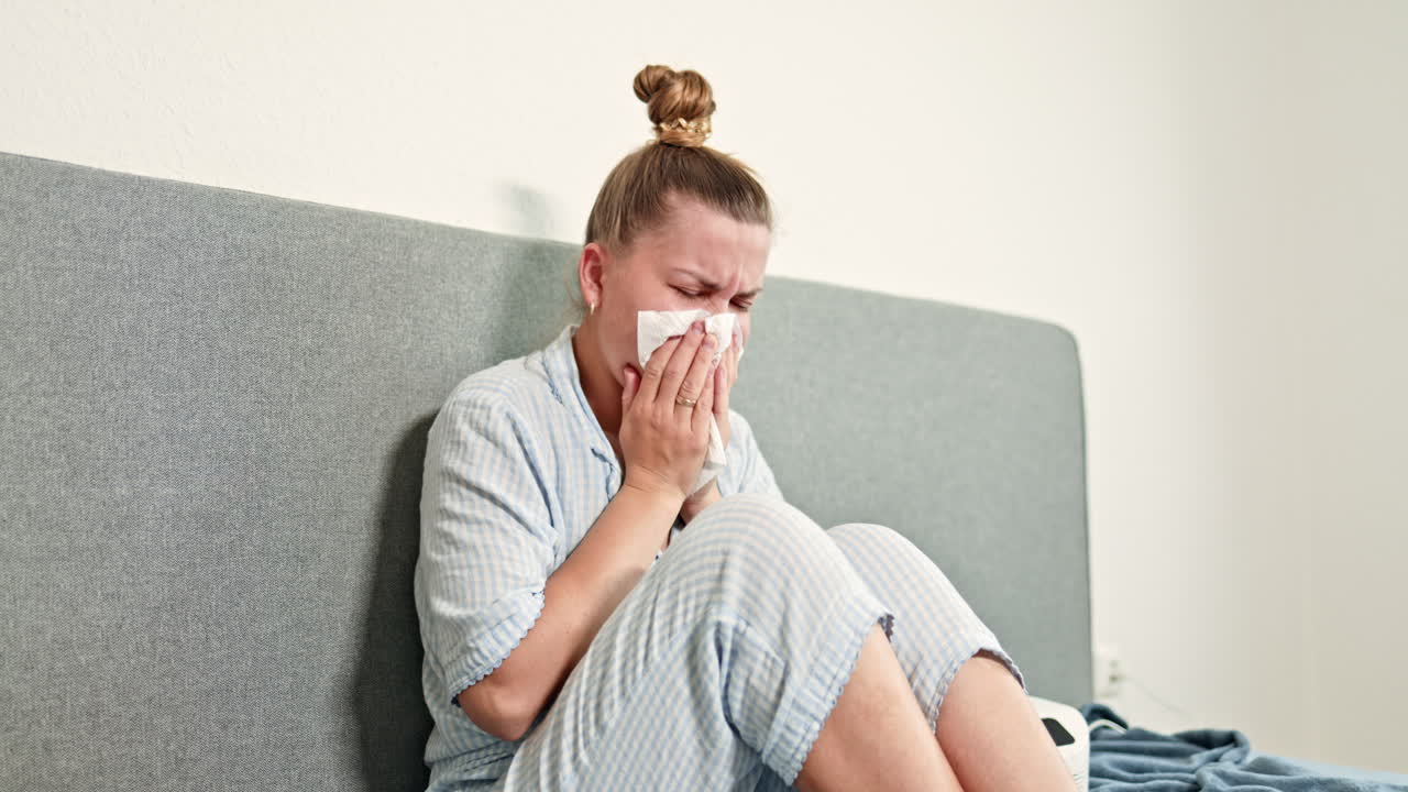 Pretty woman sitting in pajamas on bed and breathing with inhaler. Young woman treating cough with nebulizer. Woman coughing and being treated at home