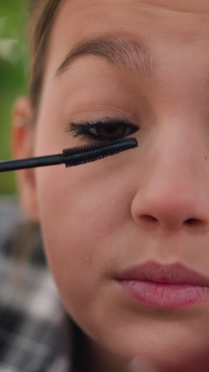 Girl carefully coats her lashes, Young girl uses gentle strokes to beautify her eyelashes gracefully, Teenager meticulously applies mascara with steady hand to enhance appearance of her eyelashes
