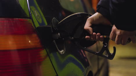 Primer-Plano-De-La-Persona-Que-Inserta-La-Boquilla-De-Gasolina-En-El-Tanque-Del-Coche,-Brillo-Fluorescente-Cálido