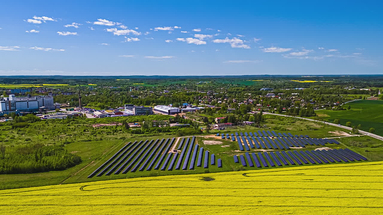 Solar Panels And Rapeseed Fields With Rural Town In The Background. Timelapse