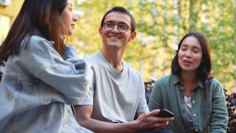 Gruppe-Von-Drei-Jungen-Japanischen-Freunden,-Die-Sich-Unterhalten,-Während-Sie-Draußen-Im-Park-Sitzen-2