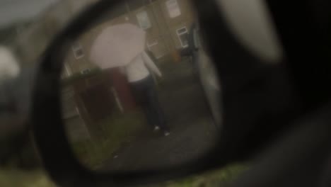 woman with umbrella in the rain pov of rear view mirror