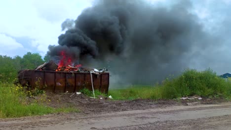 Espeso-Humo-Oscuro-Que-Sale-De-Un-Contenedor-De-Basura-En-Llamas-Lleno-De-Basura-En-Tierras-Rurales