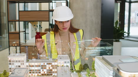 joven arquitecta confiada en hardhat analizando el modelo arquitectónico complejo de la oficina en la oficina