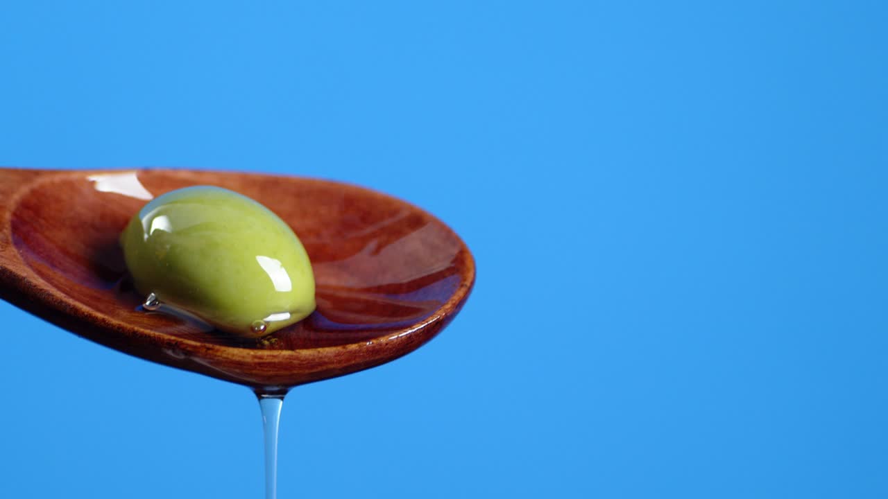 Wooden spoon with olives dripping olive oil.
