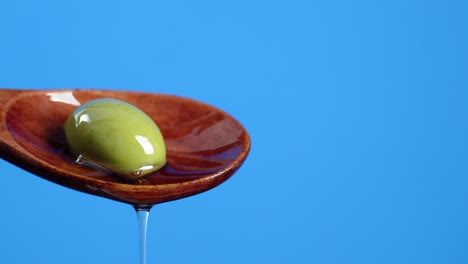 wooden spoon with olives dripping olive oil.