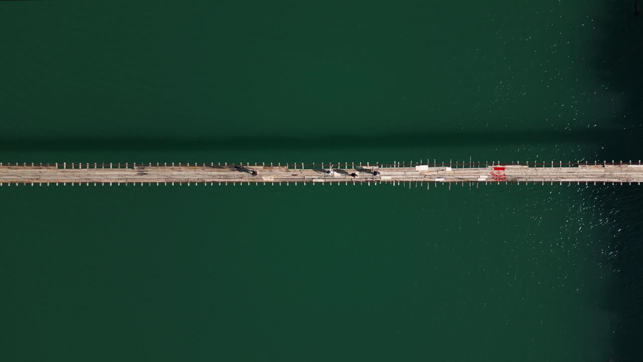 Aerial drone view of a suspension bridge over turquoise water surrounded by green mountains in Albania. Scenic and adventurous summer landscape