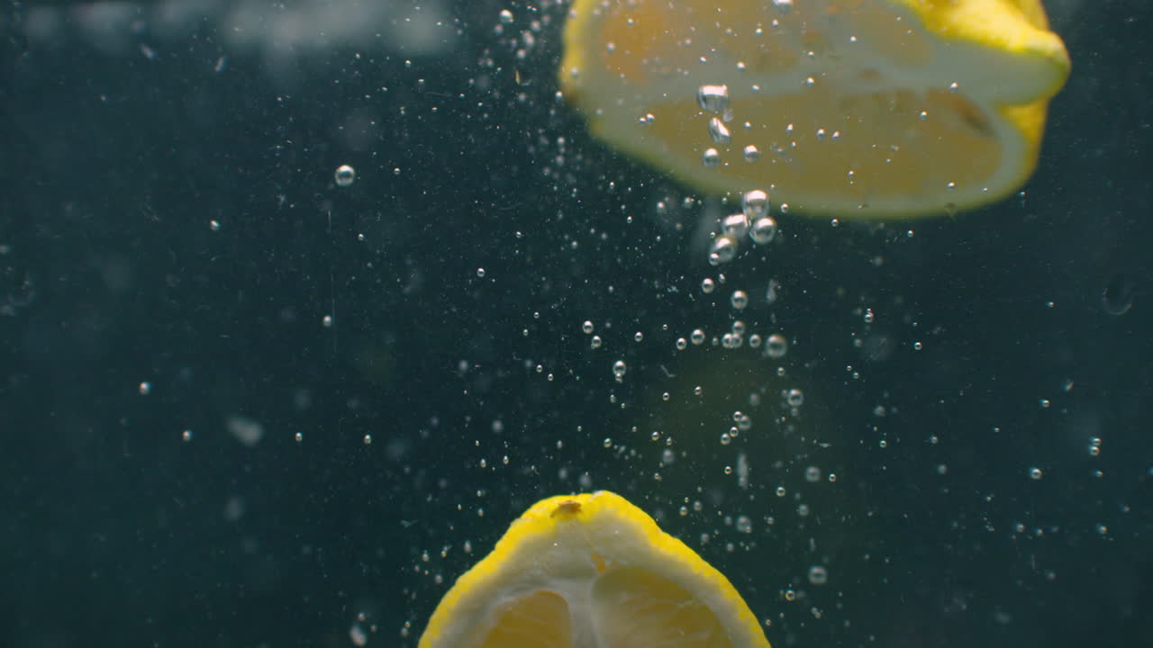varias frutas de limón caen dentro de un tanque de agua y perturban el agua. tres frutas de lemón amarillas brillantes caen adentro de un tank de agua y regresan a la superficie