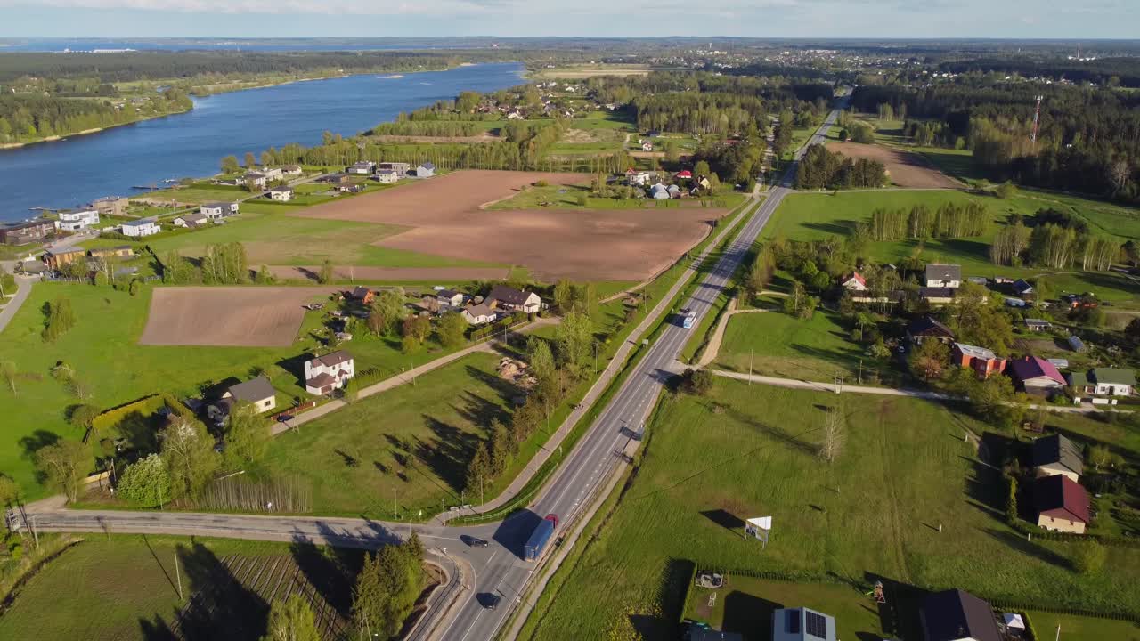 Drone pullback above peaceful suburb with road intersections, houses, and trees during spring along river