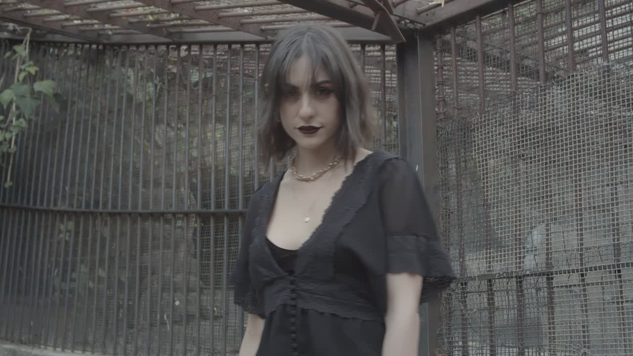 Gothic witch staring seductively into the camera lens while inside an abandoned lion cage