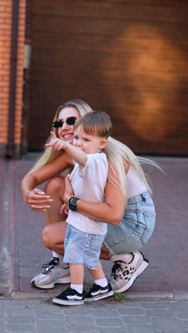 playful child runs on sunny street. a young child joyfully runs on a sunny street while a woman follows behind, creating a lively atmosphere