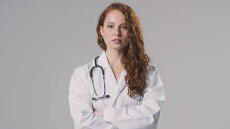 studio portrait of serious female doctor with stethoscope in white coat against plain background