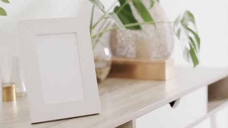 white frame with copy space on white background with plant on desk against whtie wall