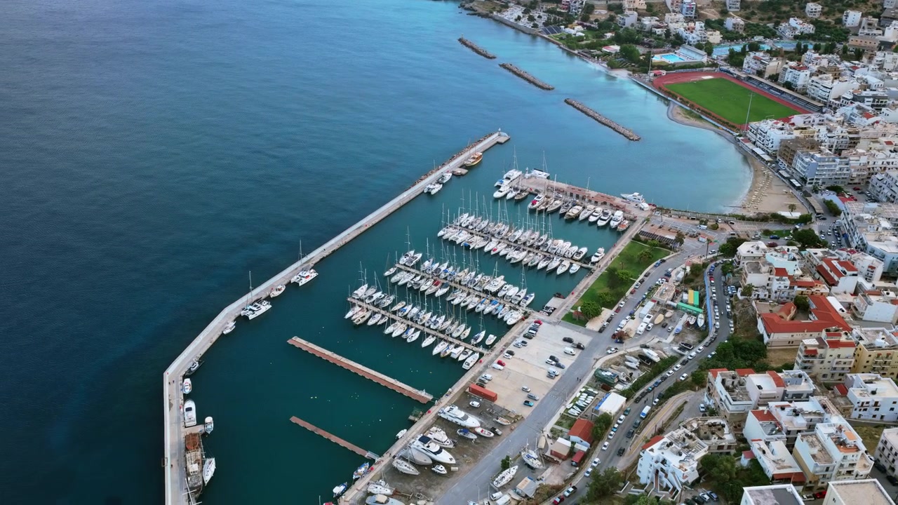 Drönarvy ovanifrån över marinan fylld med förtöjda yachter och segelbåtar intill staden, Agios Nikolaos, Grekland