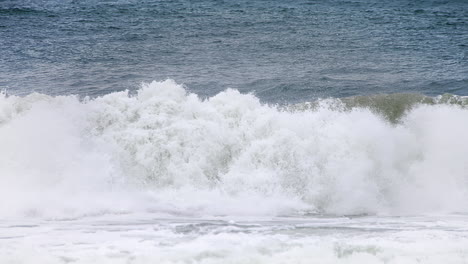 Pan-of-white-water-from-an-aggressive-crashing-wave-in-slow-motion-in-the-shore-with-a-deep-dark-blue-ocean-behind-it-and-white-water-spilling-in-high-speed-camera-120fps-4K-footage