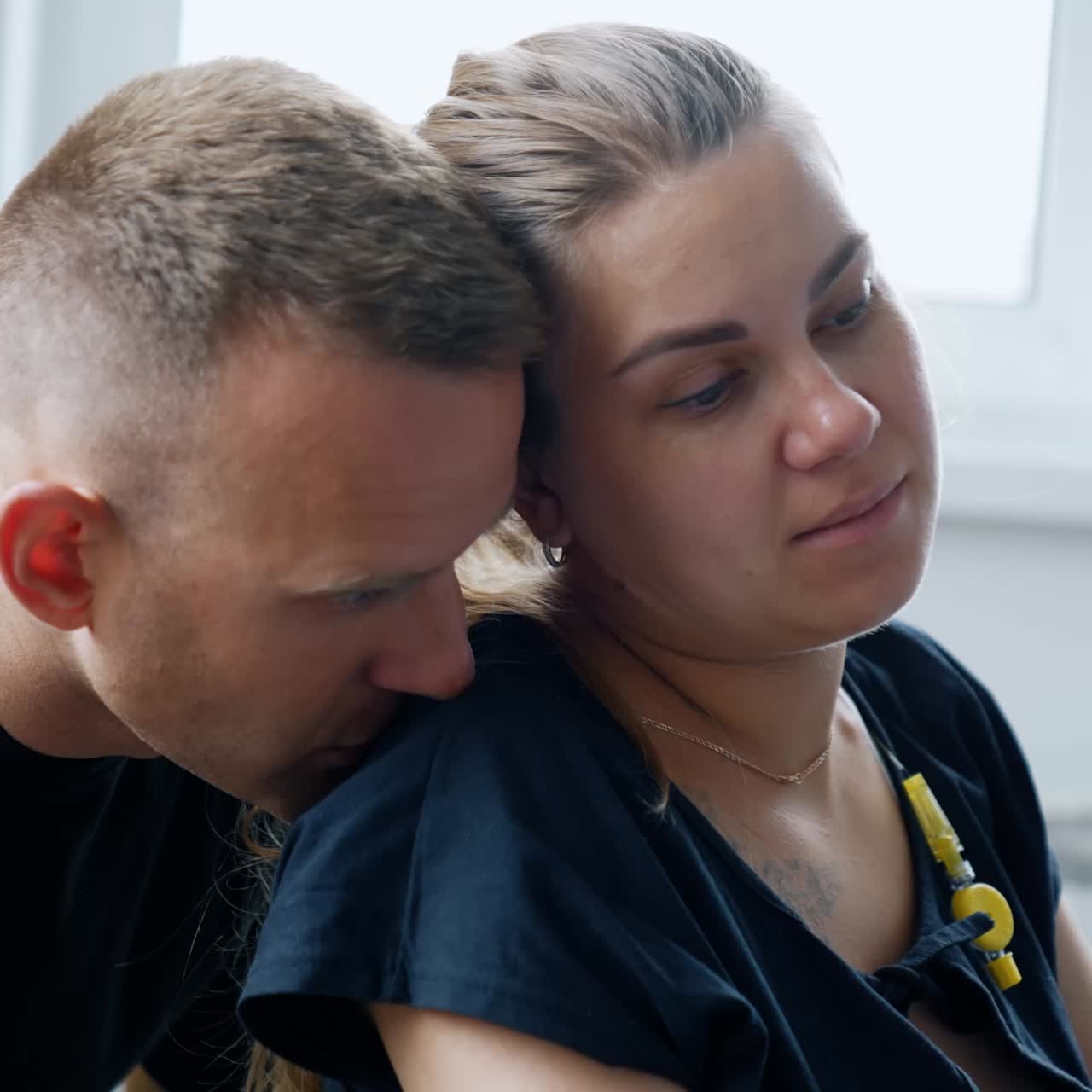 Child delivery process. Woman sits calm during the break between contractions. Husband sits behind kissing her on the shoulder. Close up
