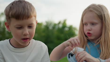 close up of boy girl watching phone together on grass, curious expressions, learning sharing content, modern digital childhood moment in park, relaxed connection between siblings and friends