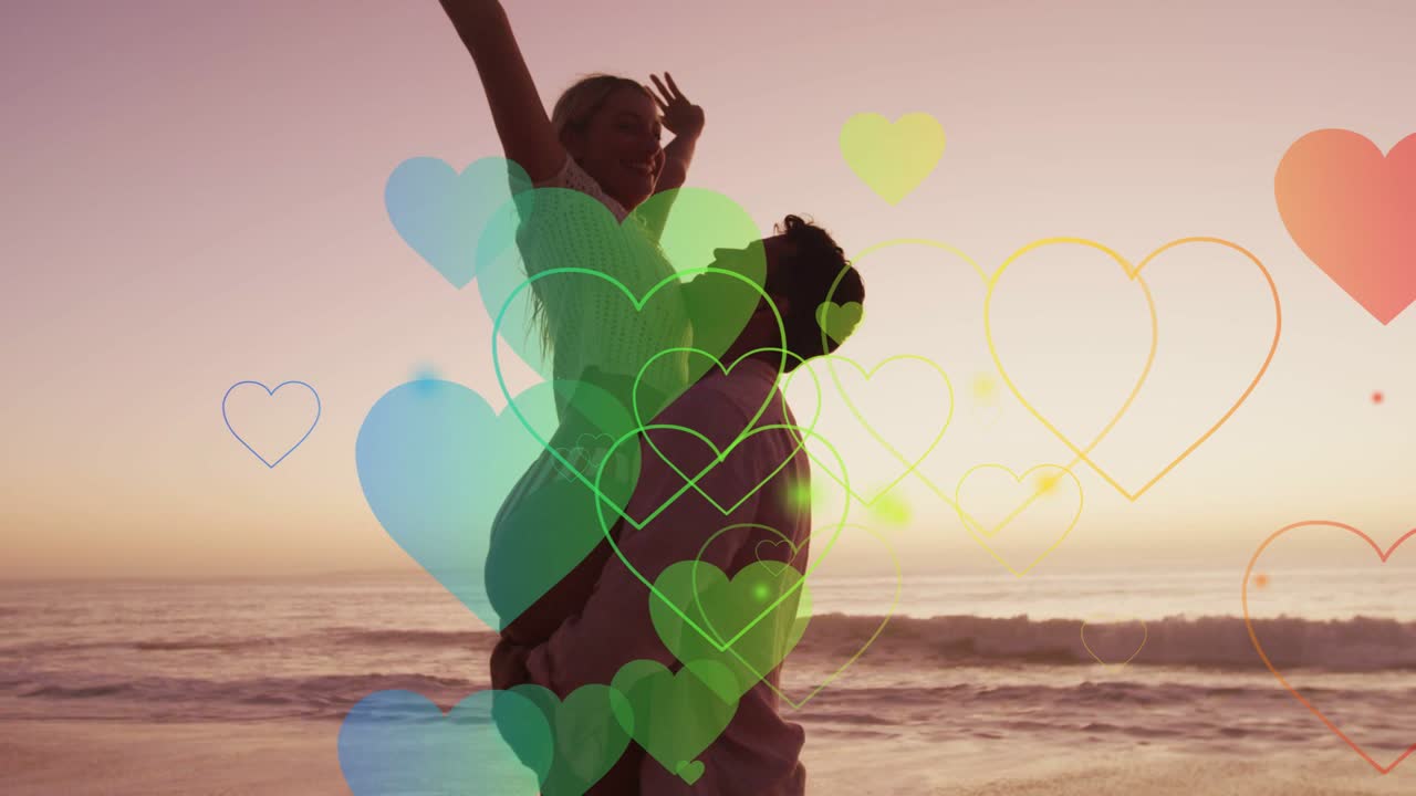 Uomo che inizia a sollevare una donna su una spiaggia al tramonto, con cuori animati che fluttuano intorno alla coppia per una promozione romantica.