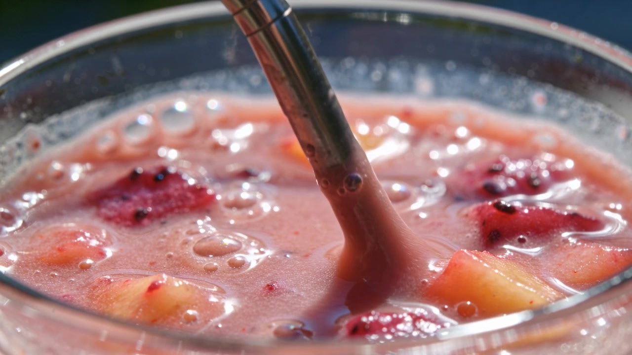 Operatore fuori campo che abbassa e guida un ugello metallico in un bicchiere in un patio con una bevanda alla frutta rosa.