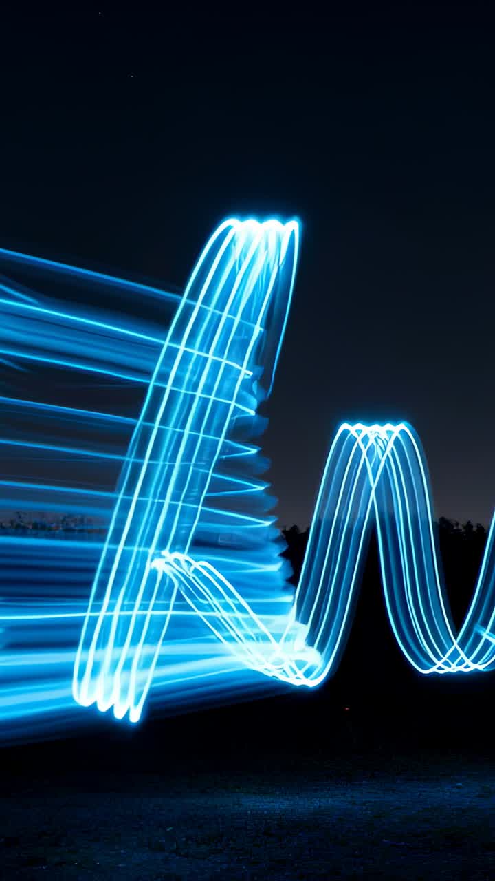Bacchetta LED in movimento che forma una spirale ciano che evolve in nastri verticali e bande sinusoidali per la fotografia notturna.