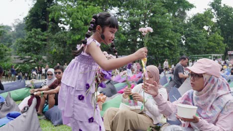 cute indonesian girl passing out flowers at an outdoor garden music festival promoting nature conservation for future generations.