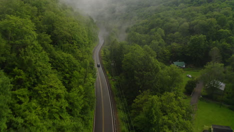 一辆单车的空中无人机在树木和雨雾的绿色森林山谷中沿着<unk>曲的山路行驶