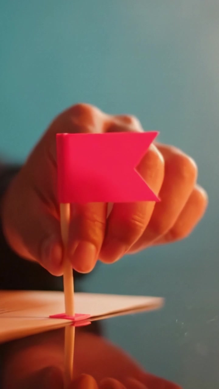 Una vista ravvicinata di una mano che posiziona una vivace bandierina rosa su una superficie, evidenziando l'attenzione alla creatività e all'espressione nelle attività artigianali quotidiane.