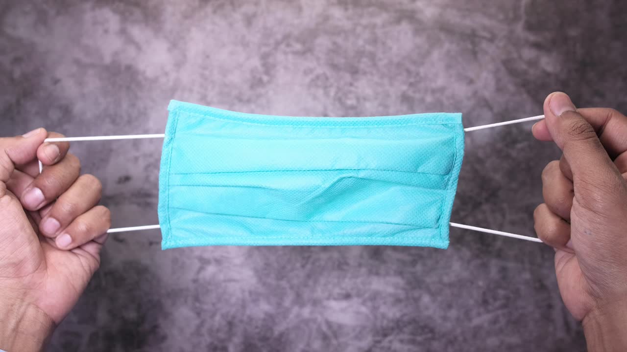 밝은 푸른색 얼굴 마스크를 들고 있는 사람