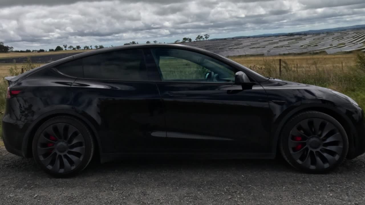 ev negro estacionado cerca de paneles solares bajo un cielo nublado