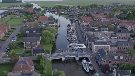 Flying-over-bridge-at-Woudsend-village-with-lot-of-small-boats-during-sunset,-aerial