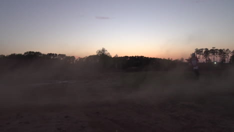 a motocross rider spins a dirt cloud then rides off, spitting dirt and dust at the camera