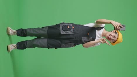 cuerpo lleno de trabajadora asiática que usa gafas de protección y casco de seguridad usando un teléfono inteligente tomando fotos mientras está de pie en el estudio de fondo de la pantalla verde