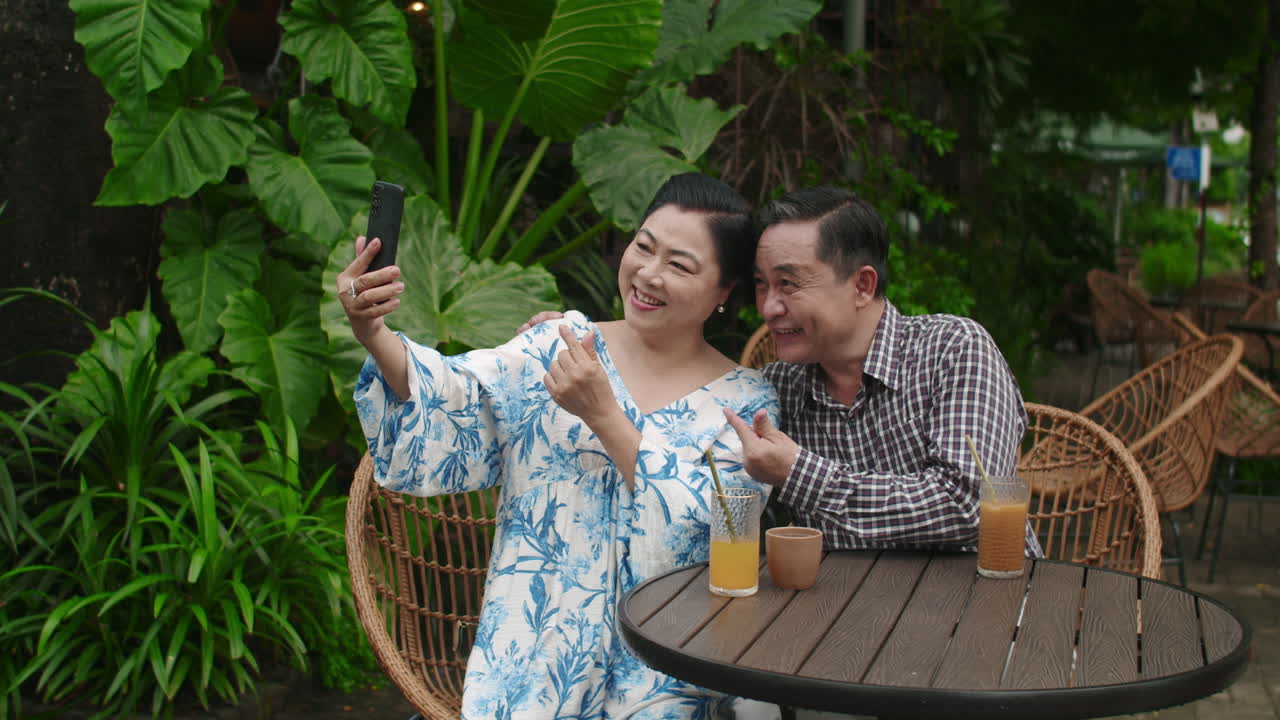 Aged Asian Spouses Taking Selfie on Smartphone in Outdoor Cafe