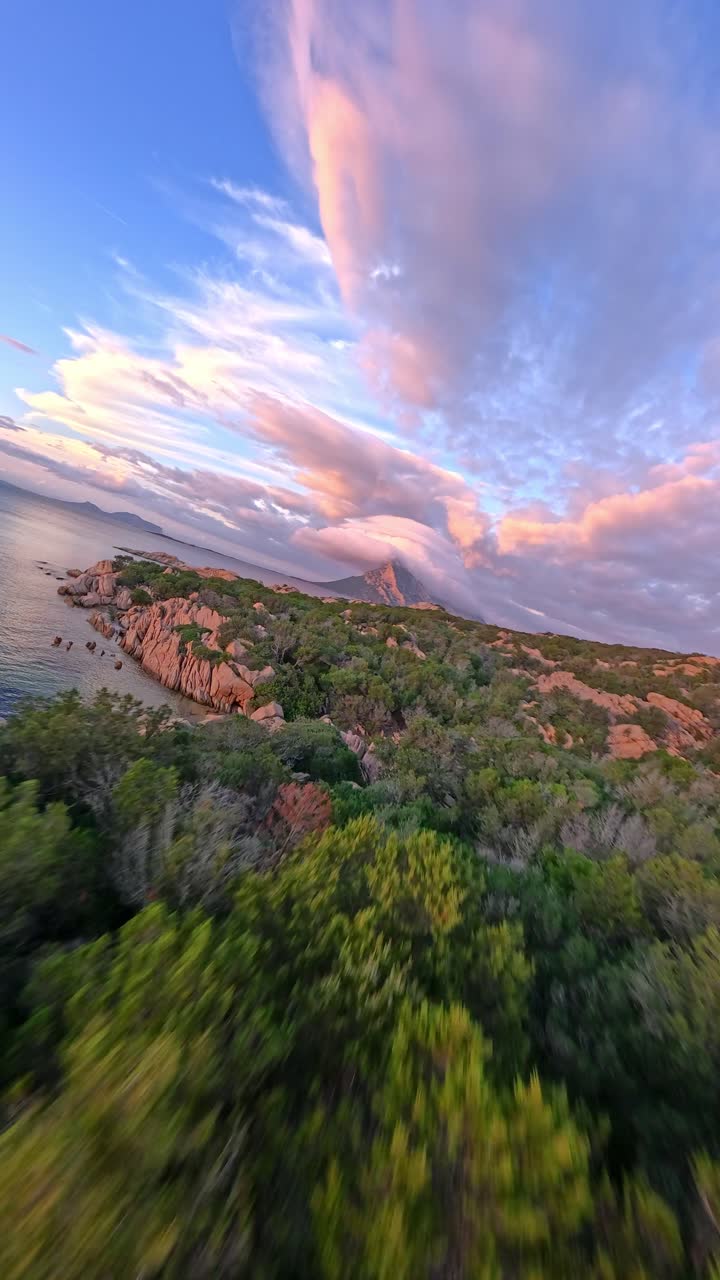 A stunning drone capture of Spiaggia delle Vacche, with Tavolara Island draped in dramatic cloud formations during sunset, showcasing the beauty of Sardinia’s coastline and the peaceful atmosphere