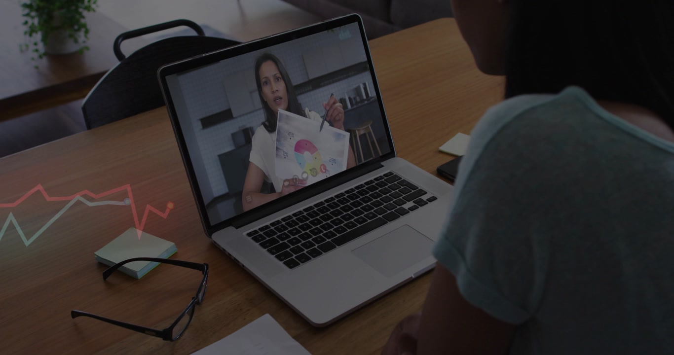 Mature woman watching remote presenter showing color charts on laptop at wood table with eyeglasses