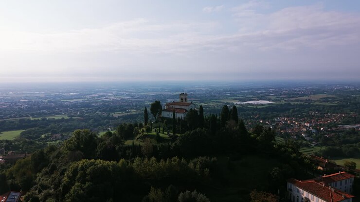 Veduta aerea di Montevecchia, Italia, che mostra il Santuario della Madonna del Carmelo arroccato in cima a una collina alberata. Il paesaggio si affaccia sulla regione Lombardia, offrendo un panorama suggestivo.