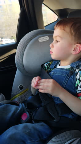 caucasian toddler riding in the car sitting in baby chair seat. child looking peacefully into window during car ride.