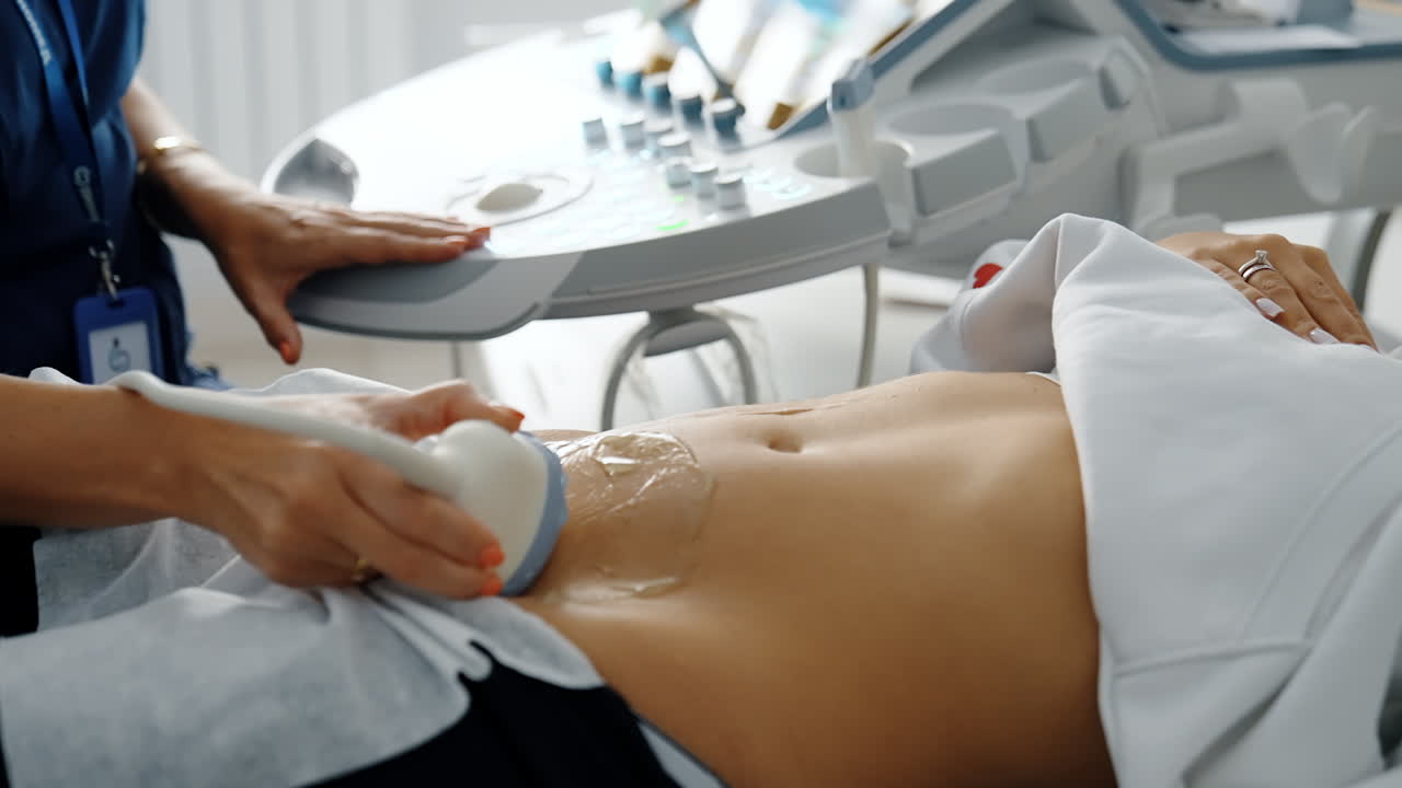 Doctor holds the ultrasound transducer low on the belly of patient. Ultrasonic examination of reproductive organs. Close up.