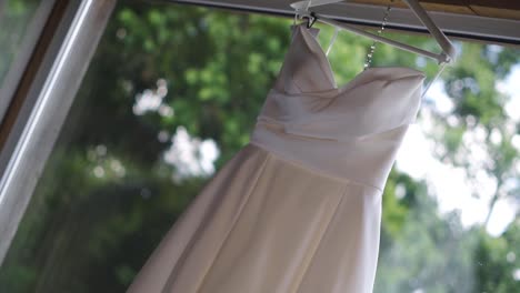 close-up of bride's white satin dress hanging on open window in room