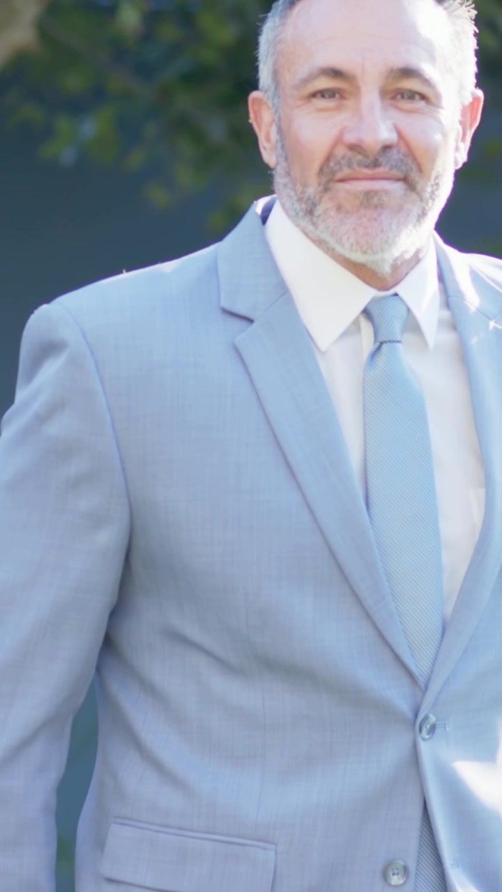 Video verticale: Uomo che cammina in abito blu che entra nel cortile, sorridendo alla telecamera per un ritratto, spazio per il testo.