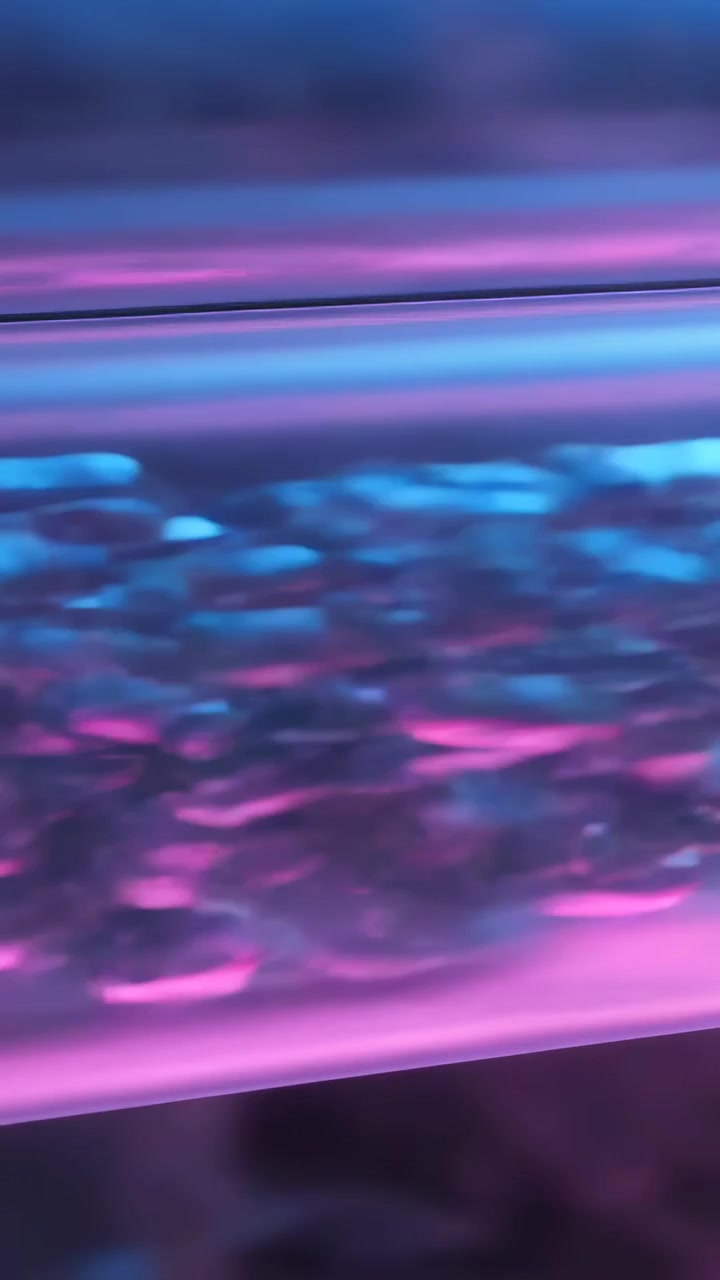 Verticale video: Schuivende camera onthult doorzichtige bellenbuis in studio, pomp creëert neon display