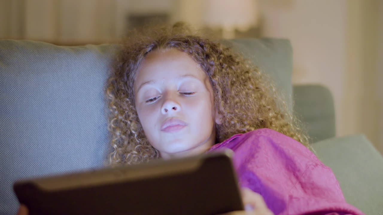 Pretty teenaged girl reading ebook before falling asleep